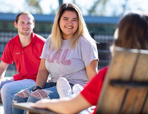 A smiling female student visits with fellow students on the patio at the Rec Center
